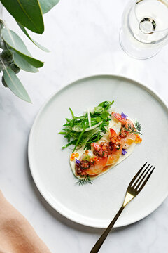 Elegant plate of poached tiger prawns with bois boudran sauce, lemon creme fraiche, salmon roe, fennel and snow pea tendril salad, on a marble surface