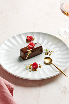 Dark chocolate glazed dessert with gold leaf, raspberries and toasted pistachios