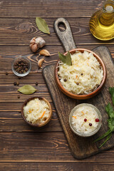 Bowls and jar of delicious sauerkraut with different spices on wooden background
