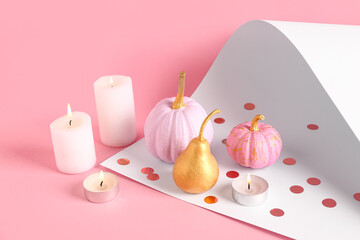 Different painted pumpkins with golden pear and burning candles on colorful background