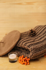 Composition with warm female clothes, burning candle and autumn decor on wooden background, closeup