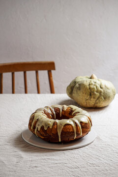 marble pumpkin bundt cake with white glaze on a plate, placed on a linen tablecloth with a rustic pumpkin in the background