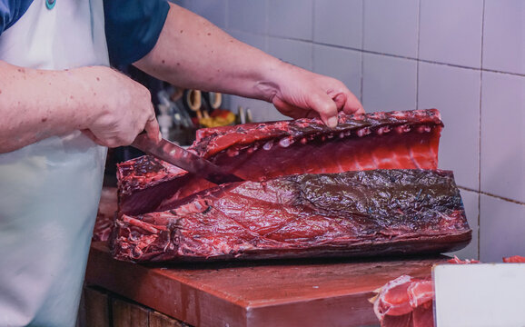 fishmonger in a white apron slices a large piece of fresh tuna at a local seafood market