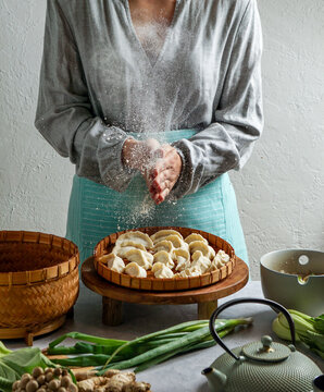 woman shef holding a bamboo tray with uncooked gyoza dumplings, bamboo steamer. teal teapot, fresh green onions, and mushrooms, Asian cuisine