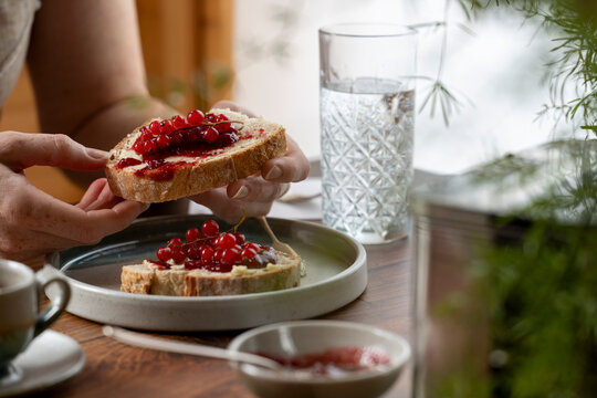 Woman holding a slice of toast topped with jam and fresh redcurrants