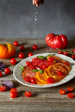 Sprinkling flakey salt on a plate of sliced heirloom tomatoes