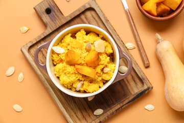 Pot of tasty millet porridge with pumpkin on orange background