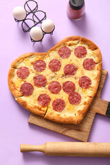 Wooden board with tasty heart shaped pizza and eggs on lilac background
