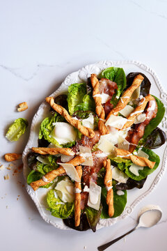 Classic Caesar Salad with Lettuce Greens, Grilled Bacon, Poached Eggs, Parmesan Cheese, and Pastry Crouton Twists.
