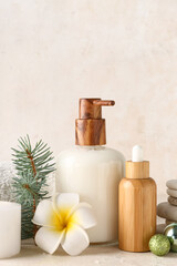 Bottles of cosmetic products, tropical flower and Christmas decor on light background, closeup