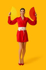 Beautiful young happy woman with fans on yellow background. Chinese New Year celebration