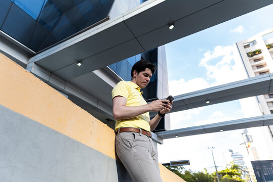 Professional man using smartphone beneath futuristic glass building