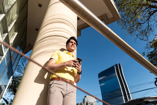 Smiling professional leaning on column with smartphone and blue sky