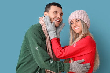 Young couple in Christmas sweaters hugging on blue background