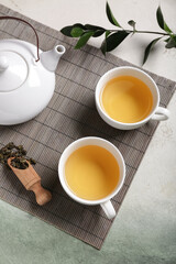 Bamboo mat with teapot, cups of tea and leaves on green grunge background