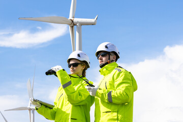 Engineer team man and woman working together with tablet, survey plan construction wind turbine sustainable clean power generator. Renewable green energy.