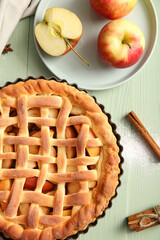 Baking dish with tasty homemade apple pie, fruits and cinnamon on green wooden background