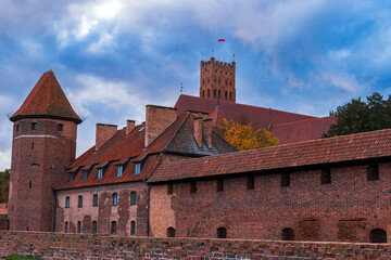 Malbork Castle's red brick walls and keep with Polish flag in autumn