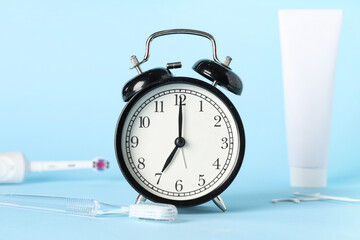 Alarm clock, toothpaste and toothbrushes on blue background