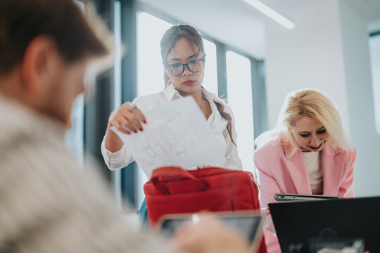 A diverse group of coworkers collaborates in a bright, modern office. One woman presents papers while others work on laptops, creating a productive and cooperative atmosphere.