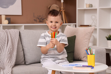 Cute little boy with felt-tip pens sitting on sofa at home