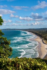 Scenic coastal view of waves and sandy beach framed by native Australian vegetation under a bright blue sky &ndash; nature landscape at Byron Bay, New South Wales, Australia