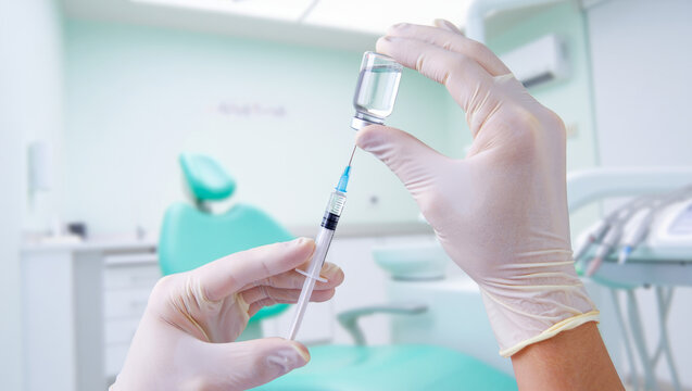 Dentist hands in gloves preparing local anesthesia injection with syringe and medicine vial for dental treatment in a blurred modern clinic background - Powered by Adobe