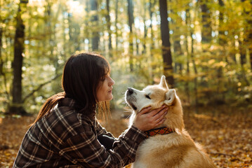 young woman walking and playing with her japanese akita puppy in autumn forest