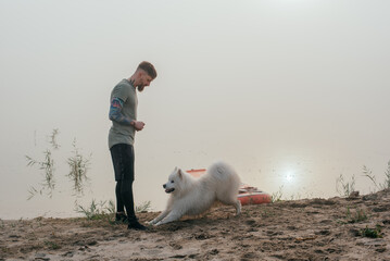 man playing with his cute samoyed dog at the lake during sunset