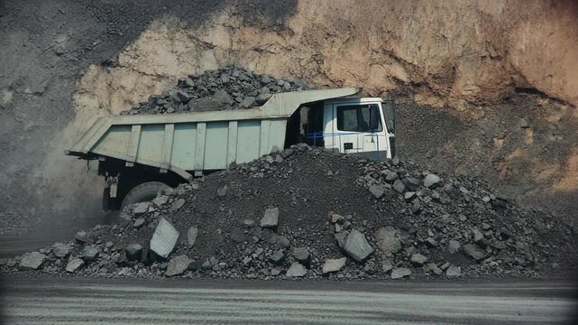 A large dumper truck unloads its cargo of stones and earth at a mining site.