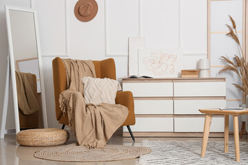 Stylish interior of living room with comfortable armchair and chest of drawers near white wall