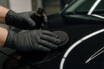 Car Detailing Precision: A skilled technician, clad in protective gloves, meticulously applies a detailing product to the sleek surface of a car.