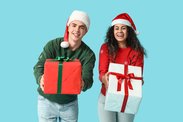 Happy young couple in Christmas sweaters with gift boxes on blue background