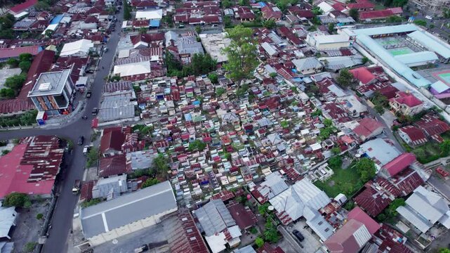 An aerial drone shot of a crowded public cemetery in the middle of Bajawa town, Indonesia. The graves are densely packed and surrounded by houses and streets.
