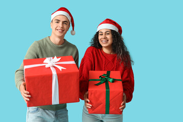 Happy young couple in Christmas sweaters with gift boxes on blue background