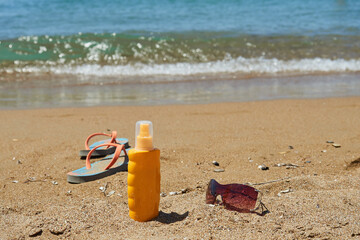 Sunglasses, a bottle of sunscreen, flip-flops against the blue sea