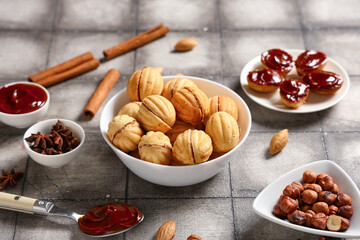 Bowls with tasty walnut shaped cookies, boiled condensed milk and ingredients on grey tiled table, closeup