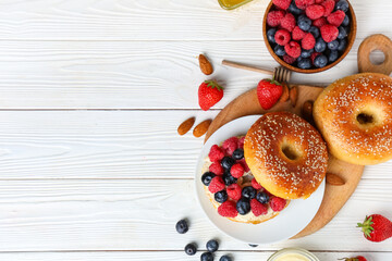 Plate of tasty bagel with butter and berries on white wooden background