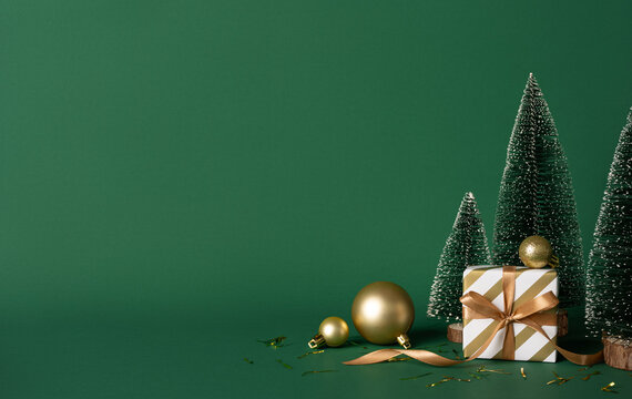 A stylish Christmas scene featuring a gold ribbon wrapped gift, tiny frosted trees, and gold ornaments set against a rich green backdrop, conveying festive warmth and New Year anticipation - Powered by Adobe