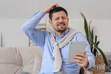 Confused young male teacher with tablet computer giving online lesson at home