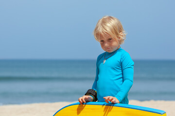 Portrait of little surfer boy with bodyboard have fun on beach, walk by white sand beach. Summer adventures, active families, parents and kids lifestyle, sports activities on school holiday with kids