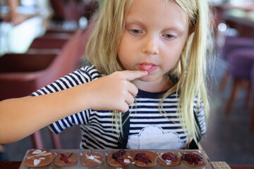 Smiling girl enjoys a sweet moment while tasting her own chocolate creation during a fun family workshop at a chocolate factory in Bali, Indonesia.