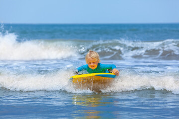 Happy young surfer boy with bodyboard have fun on beach, riding on small ocean waves. Summer adventures, active families, parents and kids lifestyle, sports activities on school holiday with kids