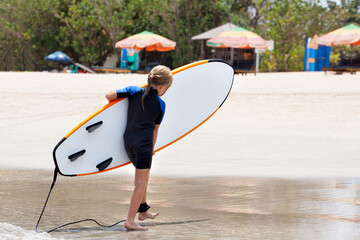 Happy young surfer girl with surfboard have fun, carry soft board on beach after surfing. Summer adventures, active families, parents and kids lifestyle, sports activities on school holiday with kids