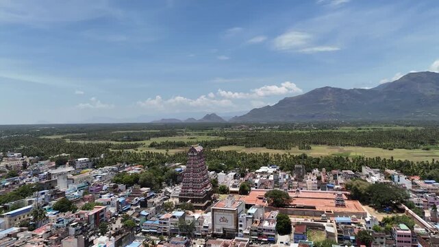 Beautiful aerial shot of Tenkasi Temple in Tamil Nadu with the Western Ghats behind, showing the ancient gopuram, green fields, and colorful town under clear blue skies.
