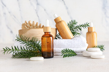 Composition with bottles of essential oil, spa accessories and fir branches on light background