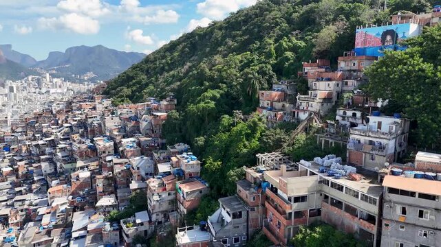 Rio de Janeiro, Brazil - 10 July 2025: Aerial view of a densely packed favela clinging to a lush green hillside contrasting with the city skyline.
