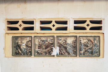 Detailed close-up showcasing decorative concrete ventilation blocks above textured glass blocks set in a aged, neutral-toned wall. The texture and design offer an architectural aesthetic.