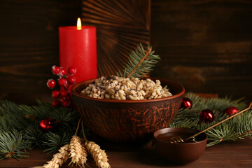 Bowl of traditional Ukrainian Kutya dish with Christmas tree branches and burning candle on wooden...