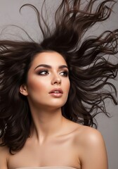 Naklejka premium Beautiful woman with flowing dark hair and elegant makeup looking up against a neutral background in a beauty portrait showcasing glamour and style